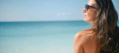Woman in sunglasses looking into the sun with ocean in front of her