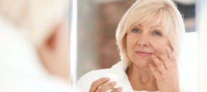 Mature woman applying moisturizing cream on face in mirror