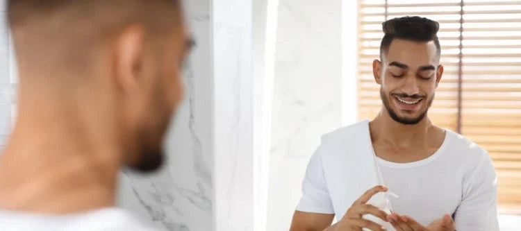 Man squirting product into hands in bathroom mirror